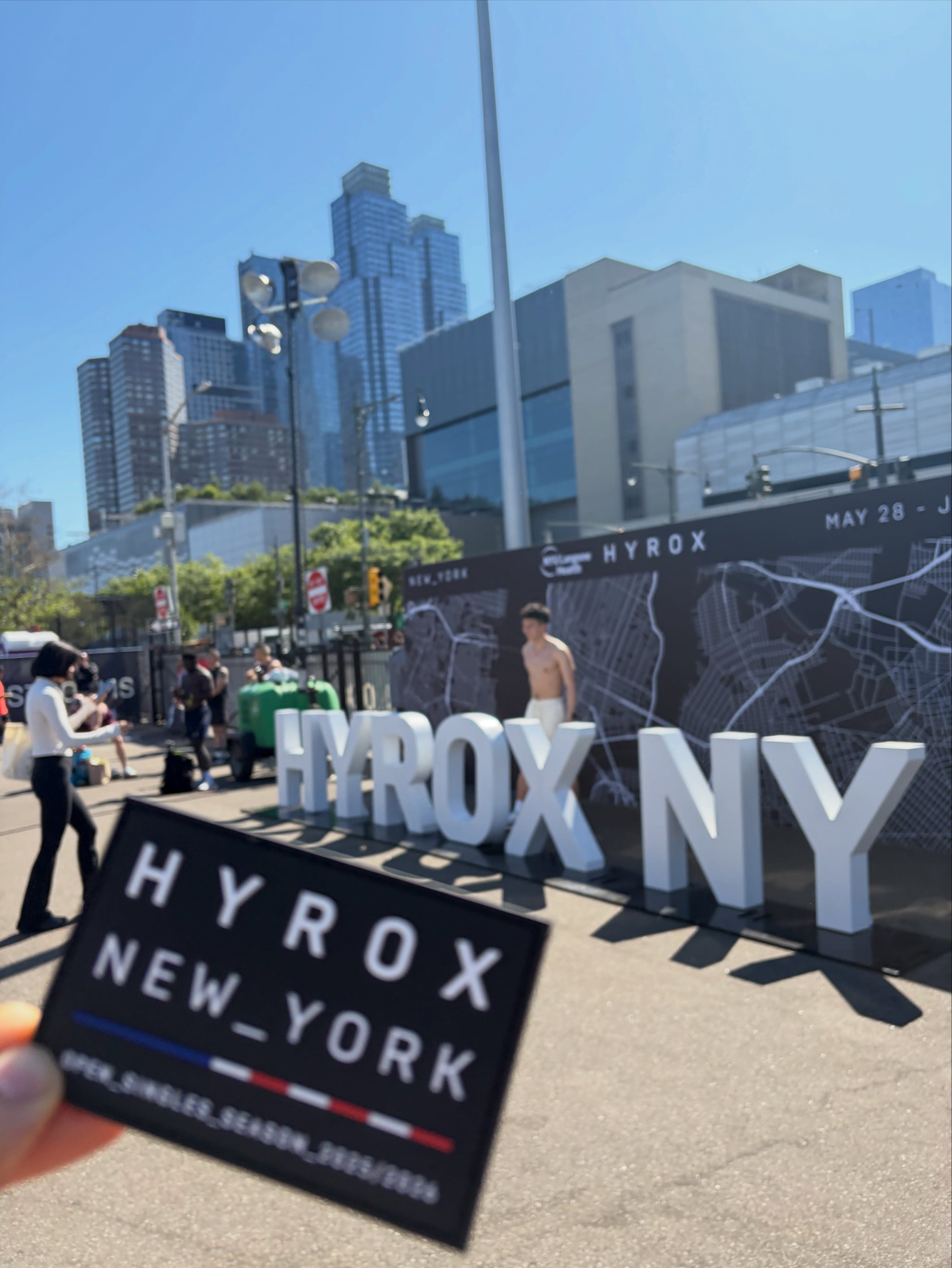 A HYROX New York season patch held up in front of the HYROX NY letters