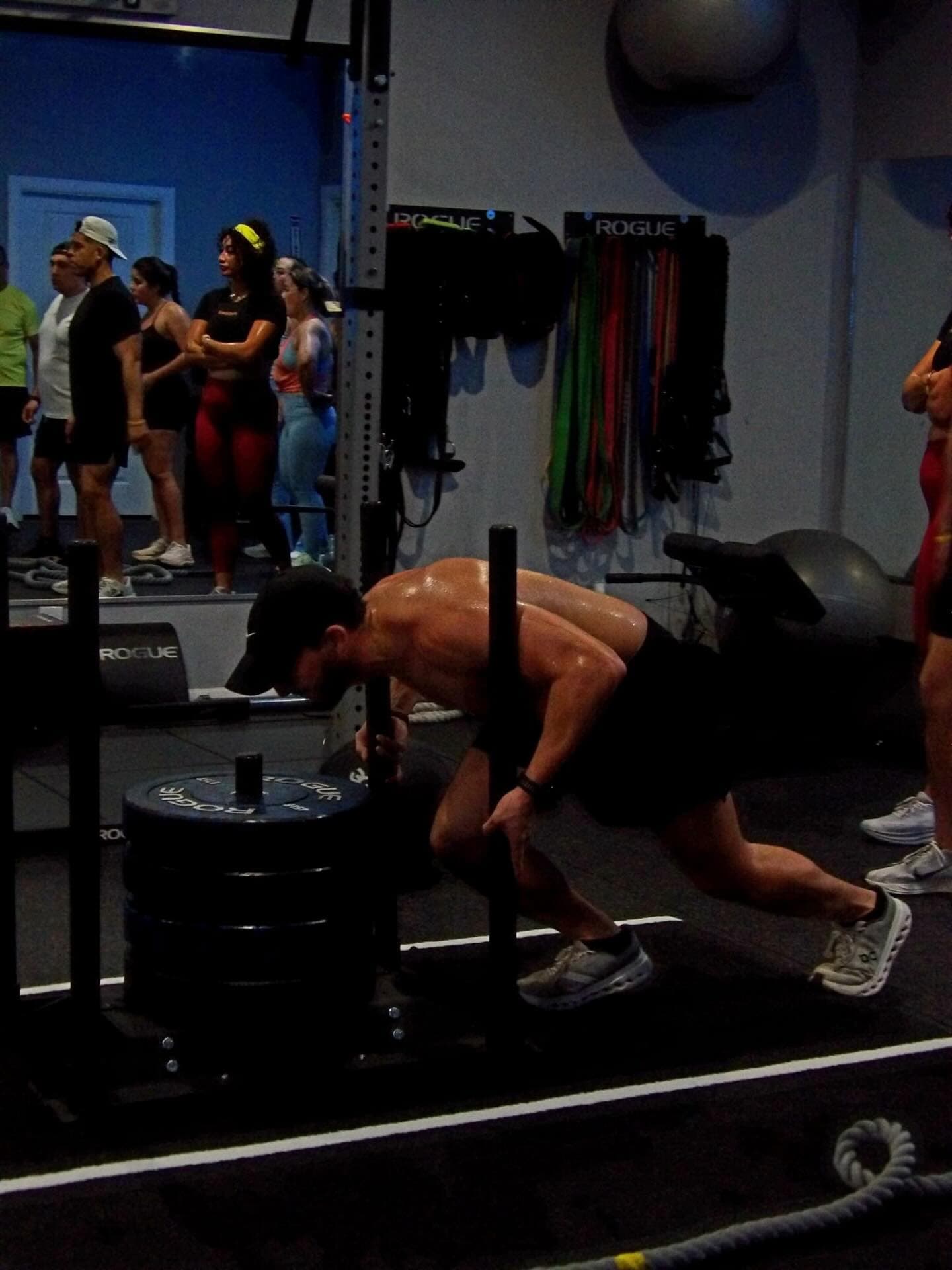 A member driving a loaded sled across the turf while the class watches
